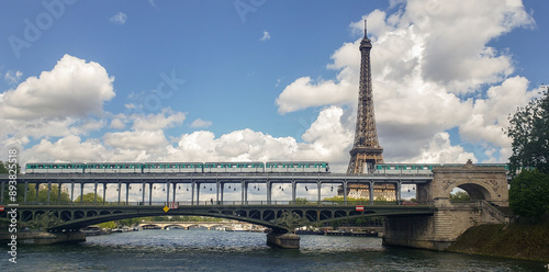 the Eiffel Tower with a bridge in the foreground and a train passing over it, under a partly cloudy sky.