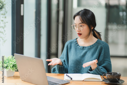 Shocked by the Screen: Young Asian woman, working remotely, reacts with surprise to her laptop, capturing the unexpected moments of online life. 