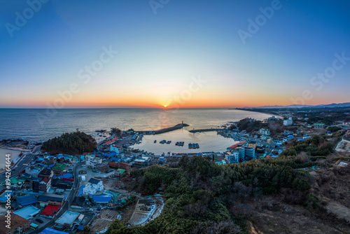 Yangyang-gun, Gangwon-do, South Korea - February 4, 2023: Aerial and panoramic view of fishing boats moored on the sea with breakwater and houses at Namae Port against rising sun 