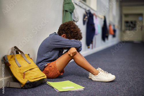 Depressed boy sitting on corridor floor at school