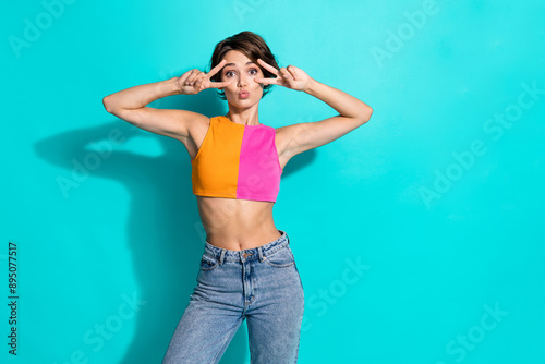Photo of excited flirty lady dressed colorful top showing two v-signs cover eyes empty space isolated turquoise color background