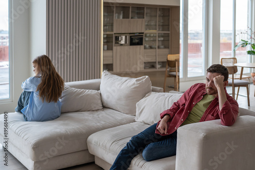 Distressed and angry couple sits on opposite ends of couch after fight, ignoring each other amidst manipulative and abusive family dynamics. Toxic silence and manipulation in couple relationship