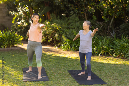 Practicing yoga, asian grandmother and granddaughter stretching on yoga mats in outdoor garden