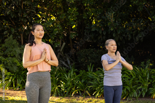 Practicing yoga, asian grandmother and granddaughter standing in prayer pose outdoors in park