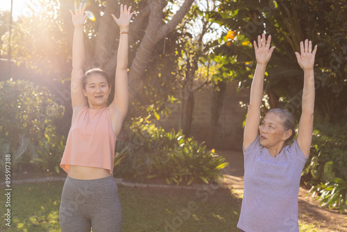 Exercising outdoors, asian grandmother and granddaughter stretching arms up in sunny garden