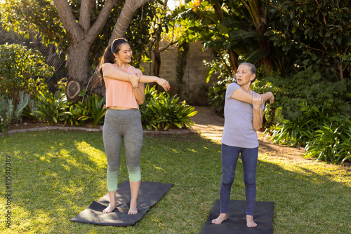 Stretching on yoga mats, asian grandmother and granddaughter exercising together in outdoor garden