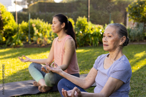 Practicing yoga, asian grandmother and granddaughter meditating on yoga mats in outdoor garden