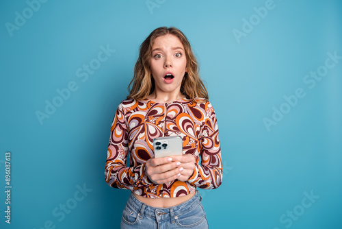 Photo of nice young girl hold phone open mouth wear top isolated on blue color background