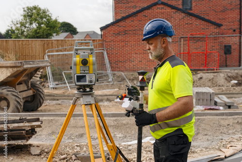 Construction Worker Using Surveying Equipment at Building Site