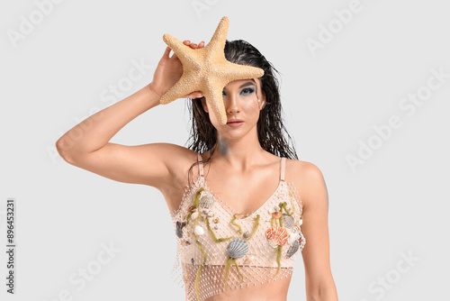 Beautiful young woman dressed as mythical mermaid with starfish on grey background