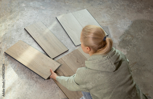 Woman Holds Luxury Vinyl Wood Samples On Concrete Floor In House. Choosing, Selecting Waterproof Flooring. Home Reconstruction. Vinyl Tiles Collection, Patterns. Interior Design Idea. Horizontal.