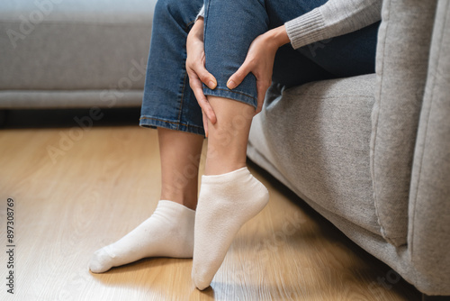 Woman get cramp on the leg sitting on sofa