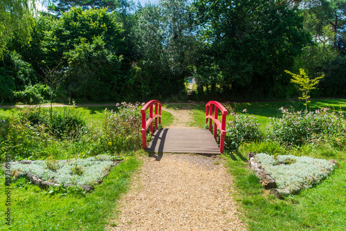 Coy Pond Gardens, Poole, UK - July 10th 2024: Red footbridge crossing the Bourne Stream in the Grade II listed gardens.