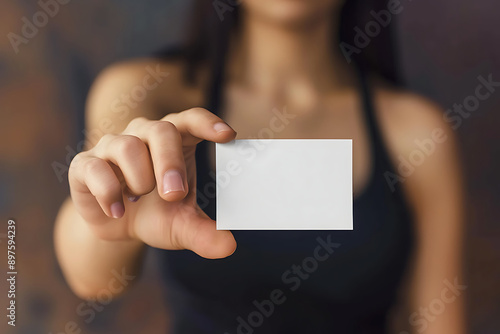 a hand and arm holding out an empty white business card with no text or design. The woman wears a black tank top with a blurred background