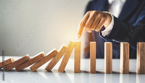 business hand halts wooden dominoes from falling over, symbolizing the prevention of a business crisis and the control of potential disruptions