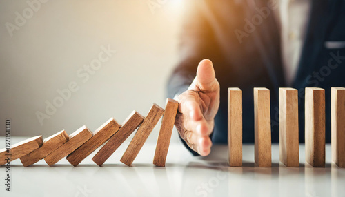 business hand halts wooden dominoes from falling over, symbolizing the prevention of a business crisis and the control of potential disruptions