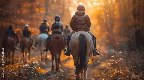 A group of individuals horse riding on a forest path during sunset in autumn, capturing the beauty of nature and the equestrian lifestyle in a serene setting.