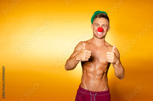 Young attractive clown man with beautiful body. Orange background.