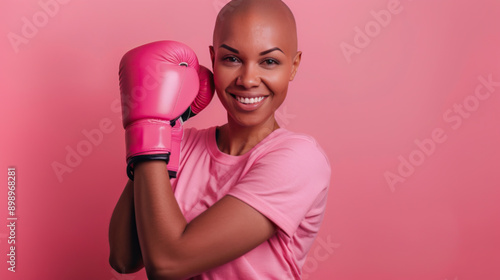 Bald beautiful woman wearing pink shirt and smiling with a boxing glove above on pink background