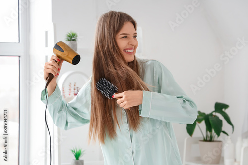 Young woman drying her hair with round brush in bathroom