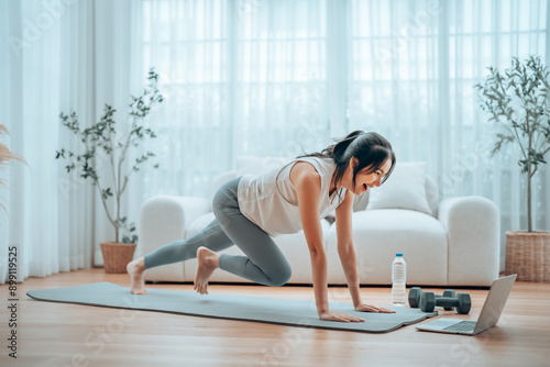 Young Asian woman doing sport exercises indoor. Beautiful girl workout at home. Athletic outfit is doing mountain climber exercises