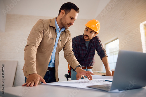 Mid adult man and construction worker examining housing plans during home remodeling process.