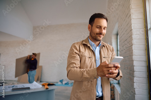 Smiling man using mobile phone during construction works at his house.