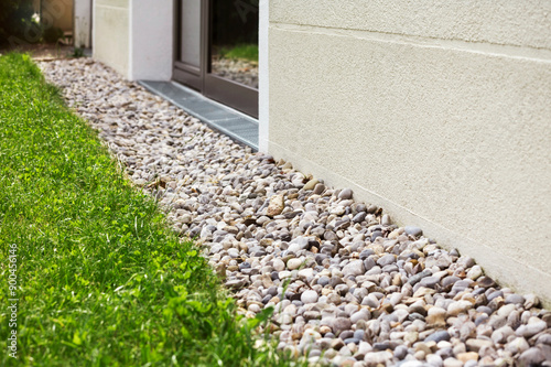 Drain Floor of Rain Water Outside House Wall. Crushed Stones Gravel Pebbles Cover as Storm Drainage System around Building. French Drain of Modern Building.