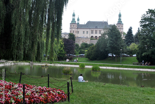 człowiek siedzący na trawie nad rzeką w parku z zamkiem w tle