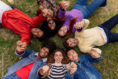 Diverse happy teenagers lying in a circle on the grass putting their hands together