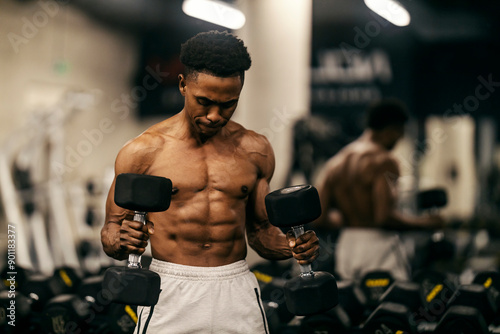 Strong powerful muscular shirtless bodybuilder doing hammer curls at gym.