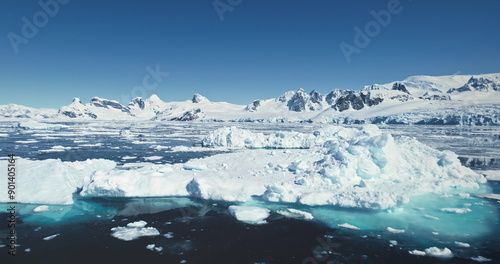 Fly over melting ice floes drifting polar ocean. Iceberg and towering snow coverd mountains in backdrop. Beauty of Antarctica landscape seascape. Ecology, climate change, global warming. Aerial shot