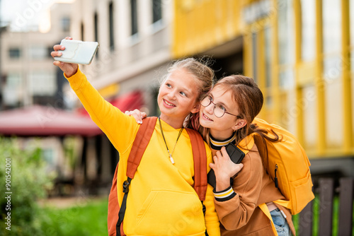 Close-up portrait of two charming schoolgirls taking selfie on the street.