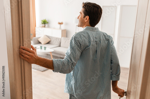 Rear back view of excited young man walking in his apartment, entering new home, happy young guy standing in doorway of modern flat, looking at design interior, coming inside, selective focus