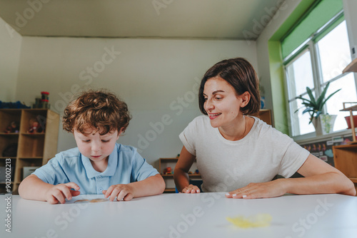 Young woman teacher playing with a boy with feathers in kindergarten