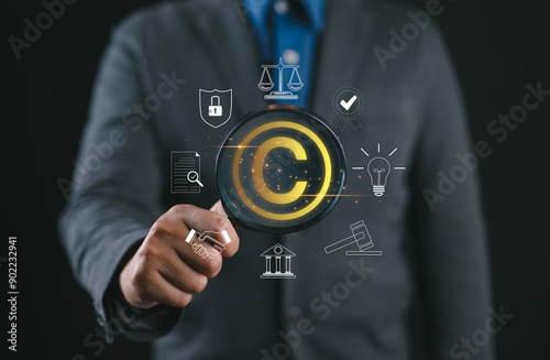 Digital copyright or patent concept. Author rights and patented intellectual property. Businessman holding a magnifying glass focuses on a copyright symbol surrounded by legal icons. trademark license