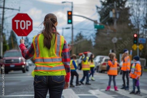 A crossing guard wearing a safety vest assists children crossing the street near a traffic light in a suburban area.