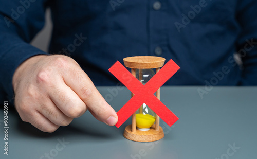 A man holds a red cross on top of an hourglass. End of time. Blocking and prohibition on further work. Refusal of additional time, termination of the contract.