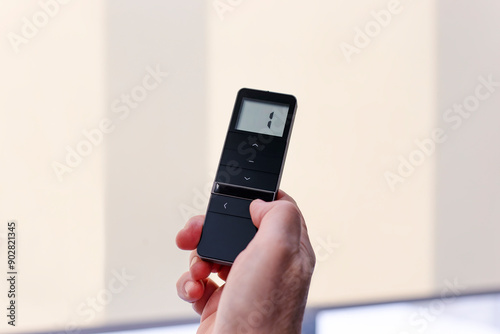 Remote control for window blinds. Man holds in his hand black remote control panel with display and operate motorized roller shades. Radio control electric blinds close-up.