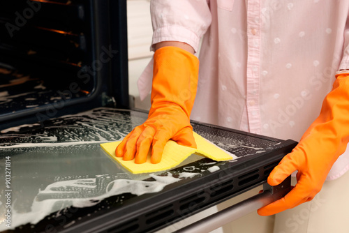 Woman cleaning oven door with rag, closeup