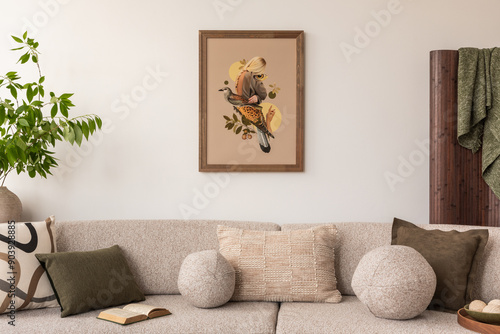 Cozy living room with a beige sofa adorned with textured and patterned pillows. A framed art piece depicting a bird and a woman hangs on the wall. A potted plant and book add to the serene atmosphere.