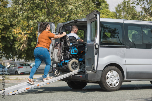 Man with a disability, a wheelchair user getting into an accessible vehicle, with the help of his girlfriend and a ramp for transportation.