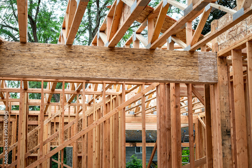 New house construction in residential neighborhood, job site detail, first floor interior wood framing installed, looking up at wood truss support beams for second floor, summer day on job site 