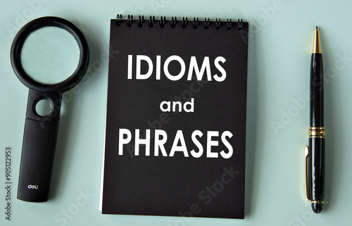 IDIOMS and PHRASES - words on a black notebook with a magnifying glass and pen in the background