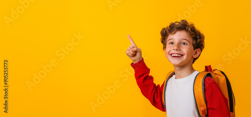 Happy smiling school boy pointing her forefinger at an empty space for promotional text, yellow background. Schoolgirl with a big smile. Back to school sales concept.