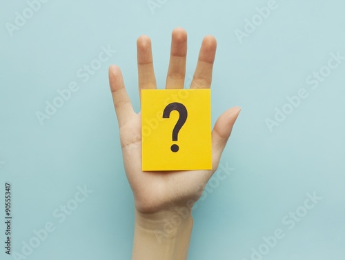 Curious Hand Holding Yellow Paper with Question Mark on Pastel Blue Background