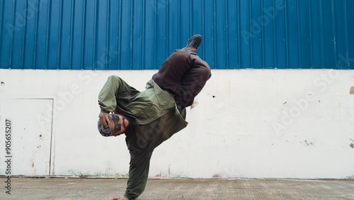 Hipster dancing b-boy foot step at street with blue wall. Asian break dancer practice street dance while stretch arms. Hip hop choreographer perform energetic dance. Outdoor sport 2024. Hiphop.