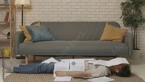 A young male college student lying on the floor of a room, doing homework or studying for exams. The young man is very tired from the stress of studying. Education Concept.