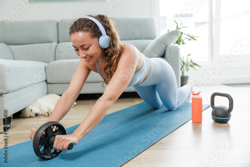 Young woman exercising at home with her pet. Listening to music with her headphones. Motivation to achieve results. Practicing sports is good for the body and mind. Healthy body, healthy mind