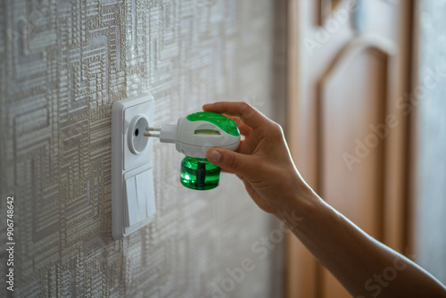 Person hand plugs mosquito repellent into the socket before going to bed. Domestic electric raptor fluid fumigator for mosquitoes protection at home, close-up. Insect repellent diffuser. 